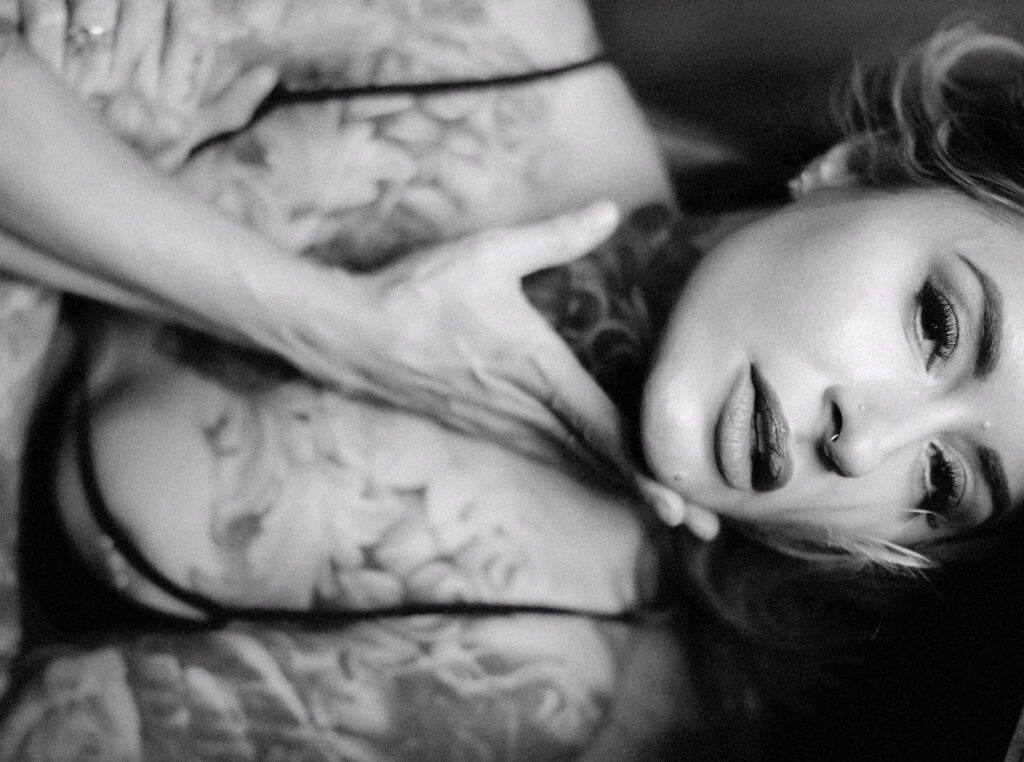 Black and white boudoir portrait of a tattooed woman lying on a bed during a Sacramento boudoir photography session.