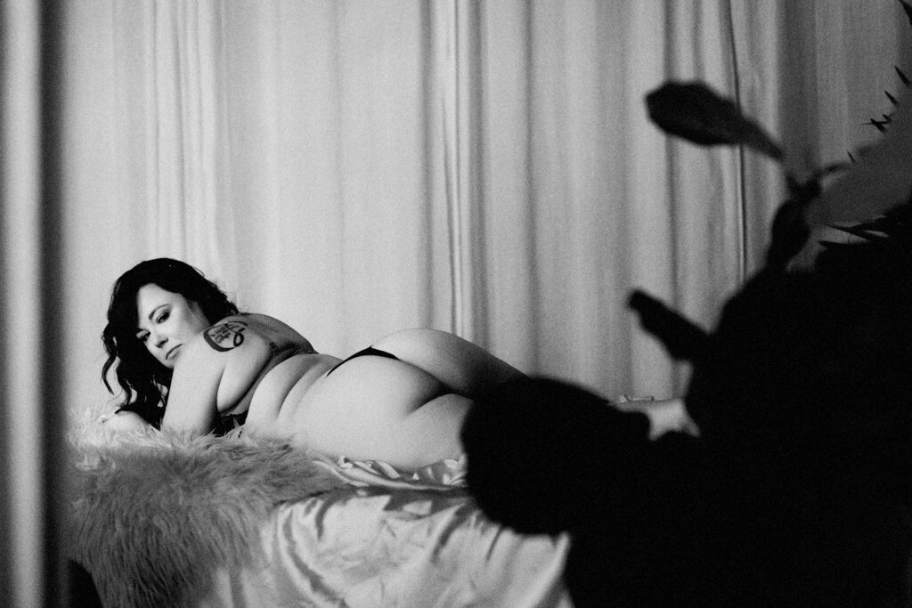 Black and white boudoir portrait of a woman posing on a bed in a Sacramento studio